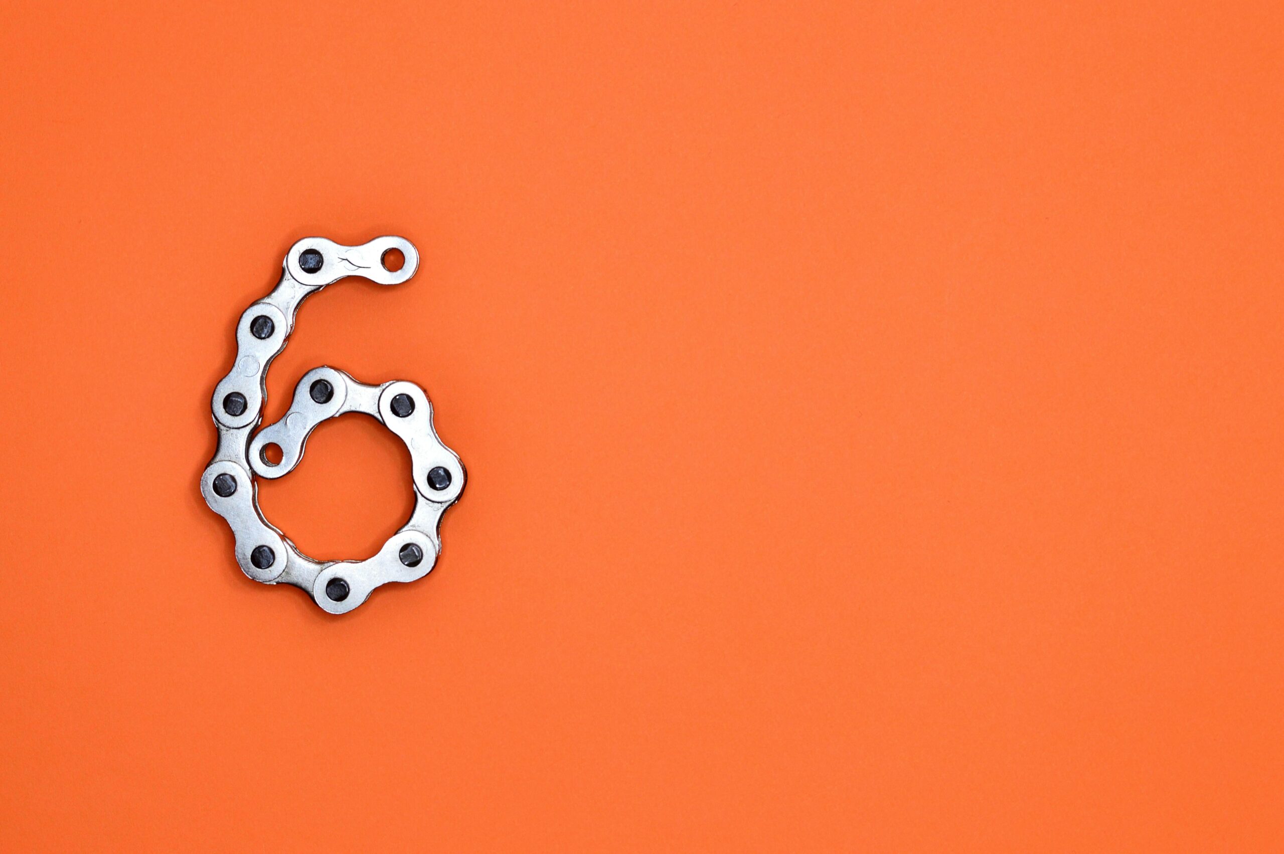 A creative display of a bike chain forming the number six against a vibrant orange backdrop.