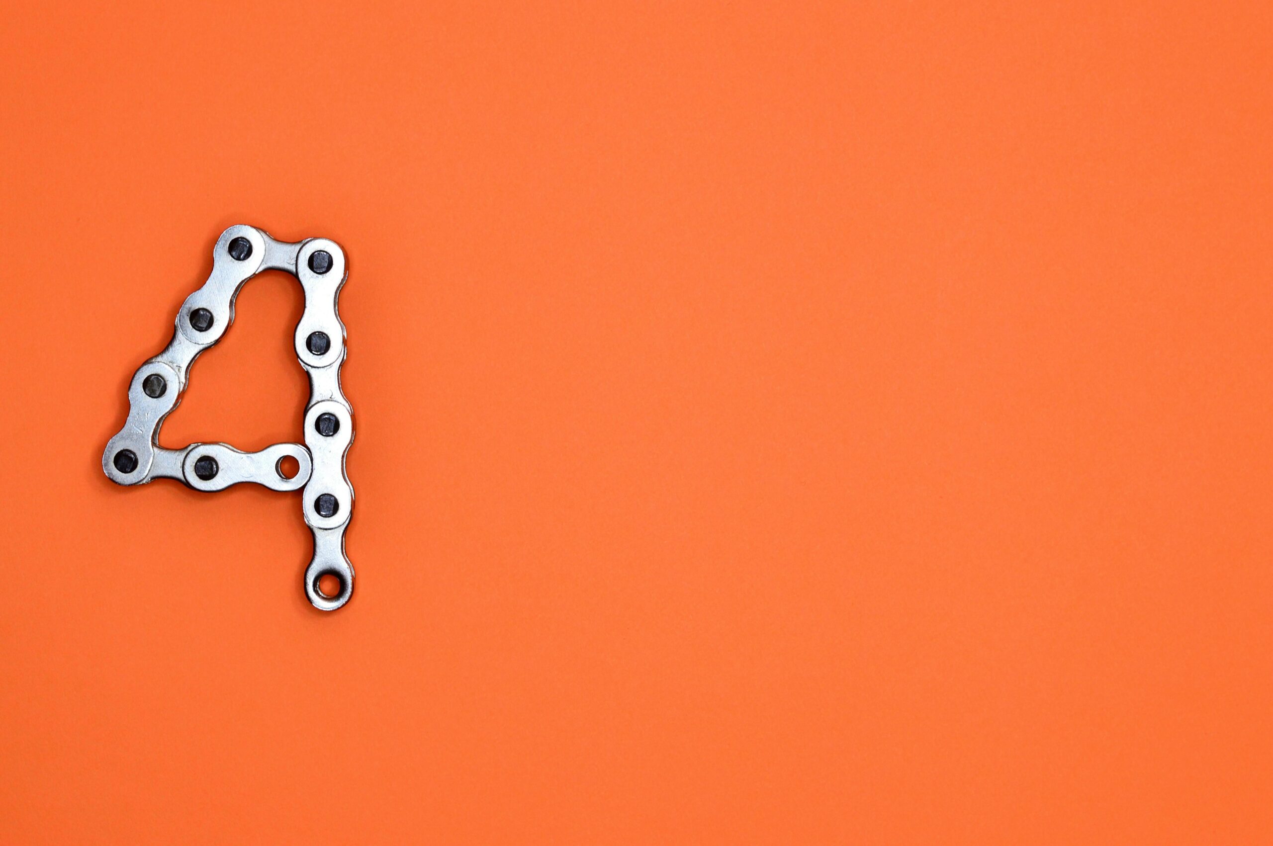 A creative design of the number four formed with a metal chain against an orange background, offering ample copy space.