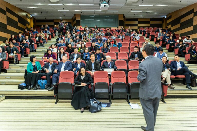 Professional setting of a business conference with attendees and a presenter in an auditorium.