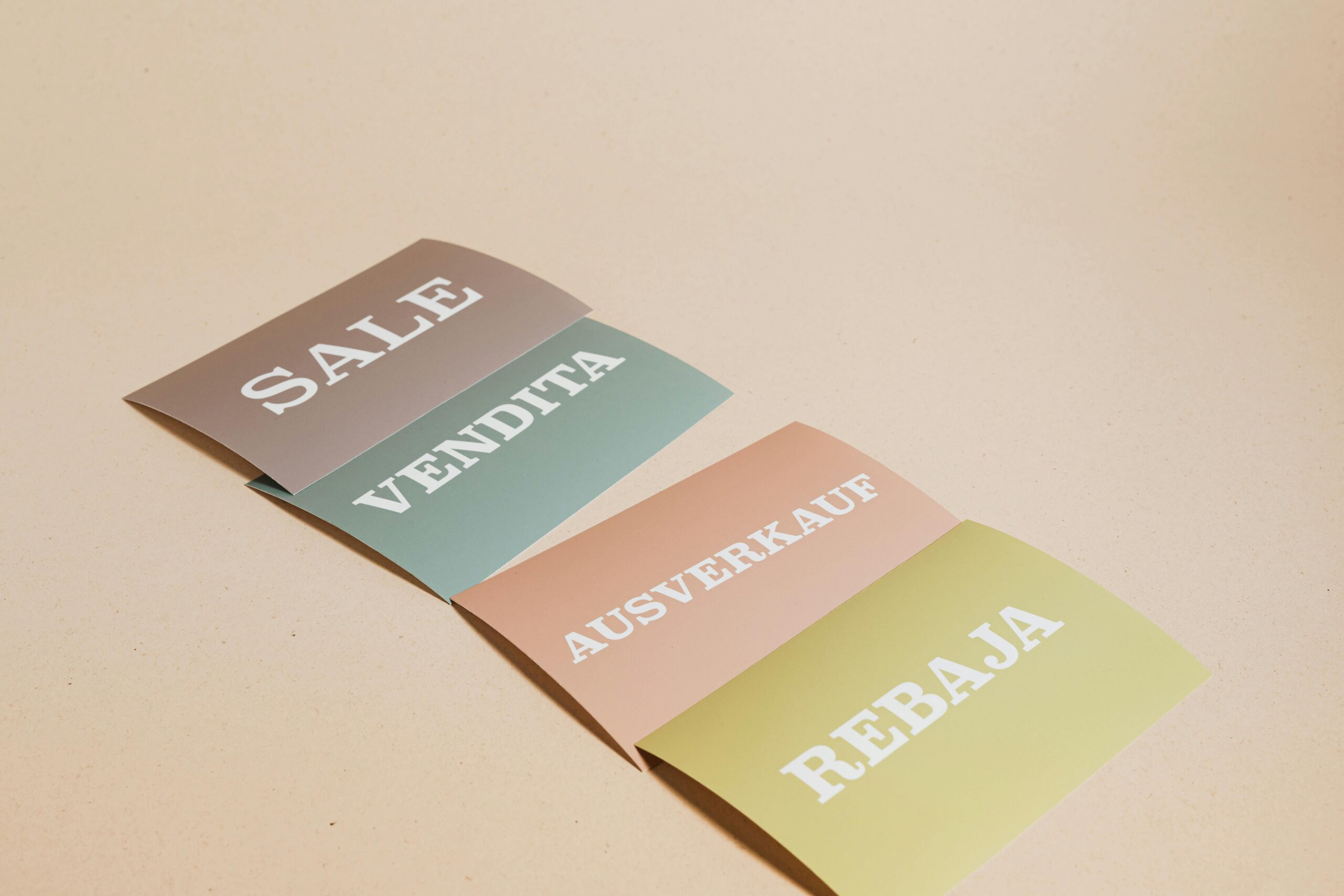 Four sale signs in different languages on a beige background, ideal for retail promotions.
